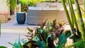 Een overdekt terras met een rieten bank en een grote plantenbak.