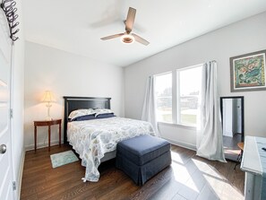 A bedroom with a bed, a nightstand, a desk, a chair, a window, and a ceiling fan.