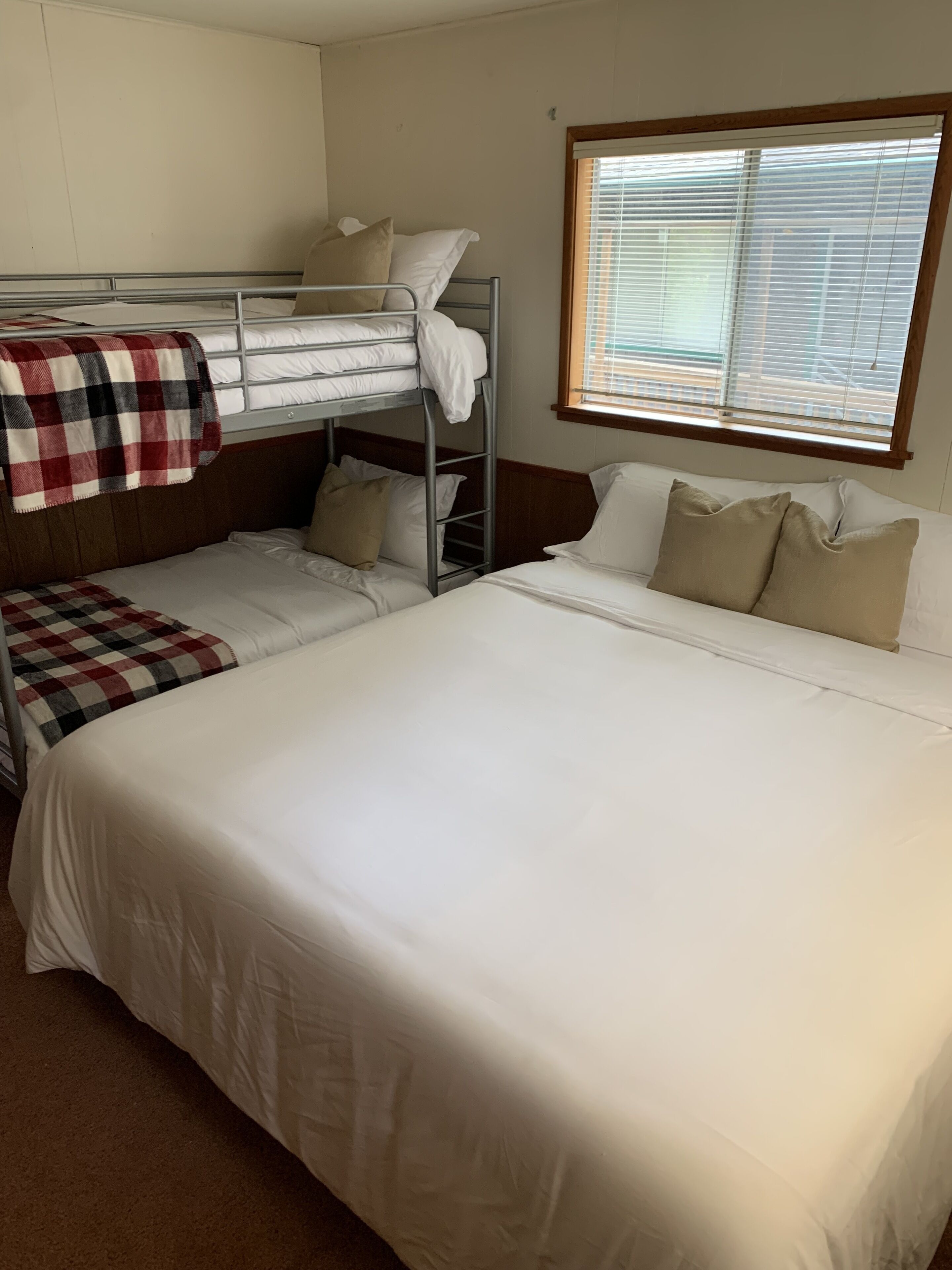 A room with bunk beds, a large bed, and a window with blinds.