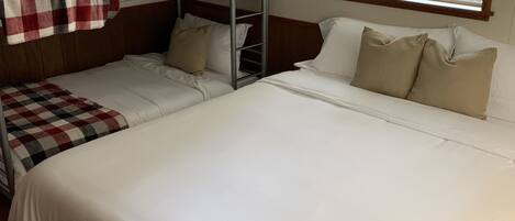 A room with bunk beds, a large bed, and a window with blinds.