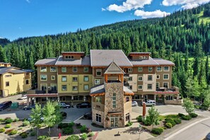 A multi-story hotel with a stone tower entrance, surrounded by a parking area and lush greenery.