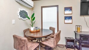 A dining area with a round table, cushioned chairs, a potted plant, and framed artwork on the wall. - Bluebonnet Tiny Home ~ HOT TUB (Willis)