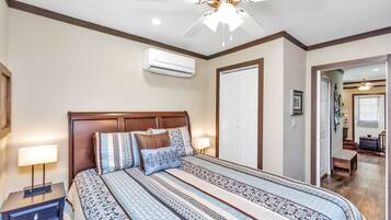 A hotel room with a large bed, a ceiling fan, an air conditioning unit, a nightstand, and a door leading to another room.