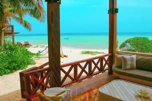 Uitzicht op het strand vanaf een houten terras met een bank en stoelen, met zicht op de oceaan.