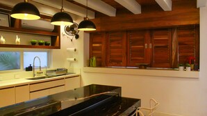 A modern kitchen with a black countertop, wooden cabinets, and pendant lights. - Esciros Luxury Villa (Progreso)