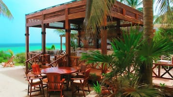 Un área de estar al aire libre con mesas y sillas de madera, con vista a la playa.