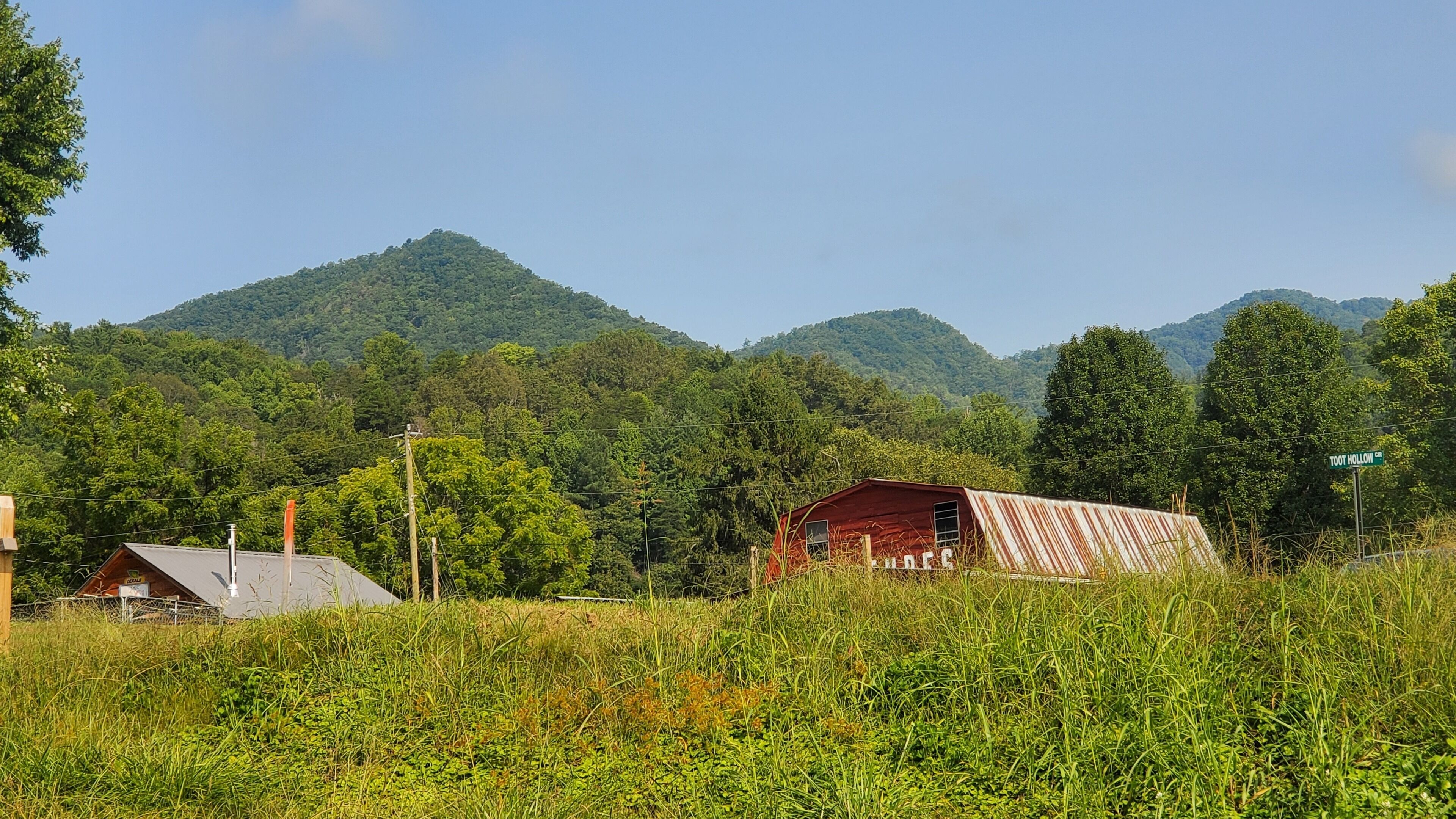 A rural landscape with a red barn, a smaller grey building, and a sign reading "Toot Hollow CR."
