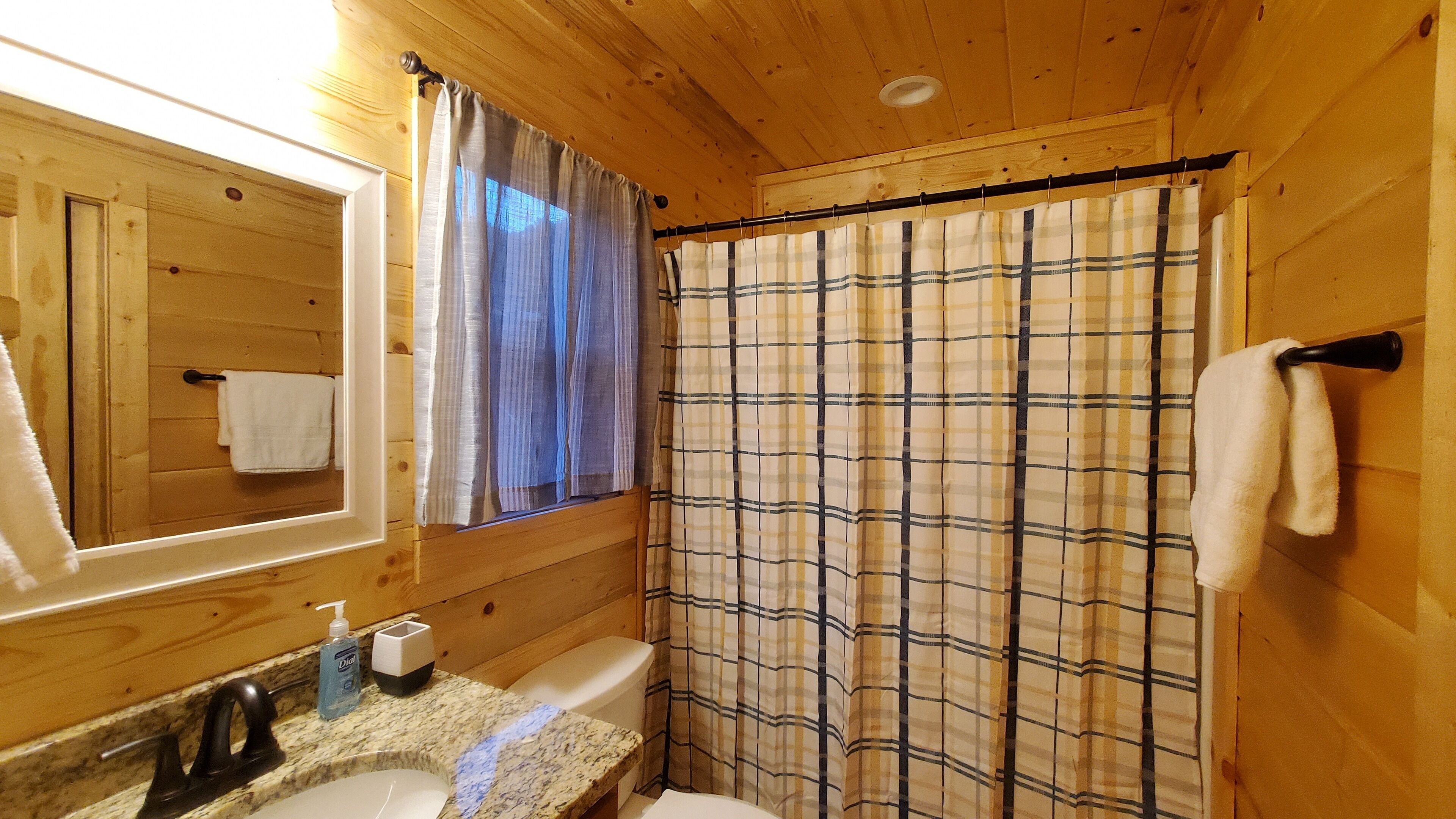 Baño de cabaña de madera con lavamanos, espejo y cortina de ducha.
