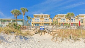 Un hotel frente a la playa con varios balcones, un paseo de madera y palmeras.