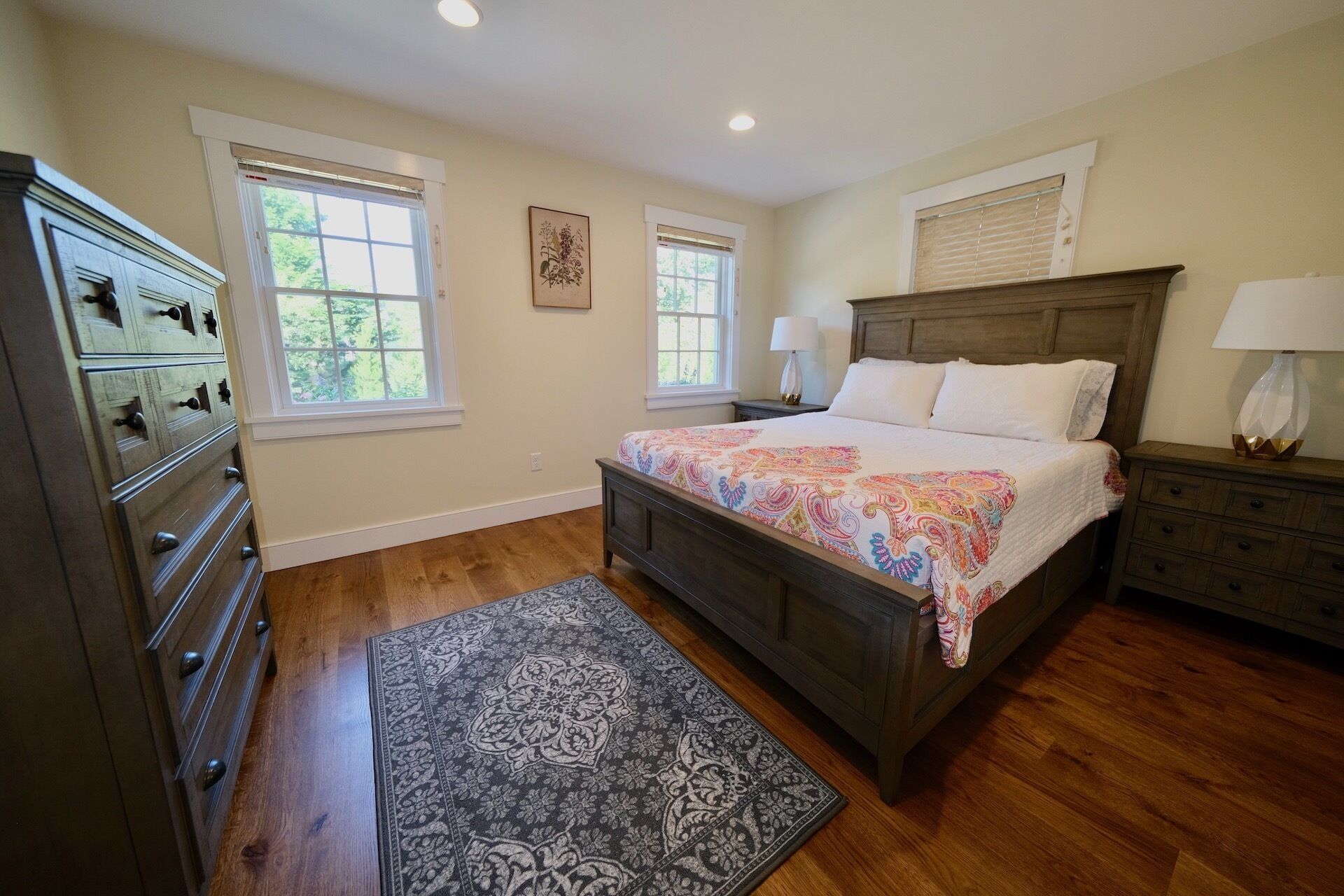 A bedroom with a wooden bed, two bedside tables, a dresser, and a rug.