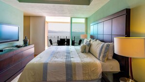 A hotel room with a bed, a TV, a desk with a lamp, and a view of the sea. - Stunning views over the bay from Grand Venetian  (Puerto Vallarta)