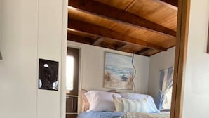 Une chambre à coucher avec un lit, un plafond en bois, un tableau et une petite table ornée d’objets décoratifs.