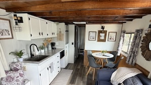 Une cuisine compacte avec des meubles blancs, un évier noir et un coin repas comprenant un canapé bleu et une petite table.