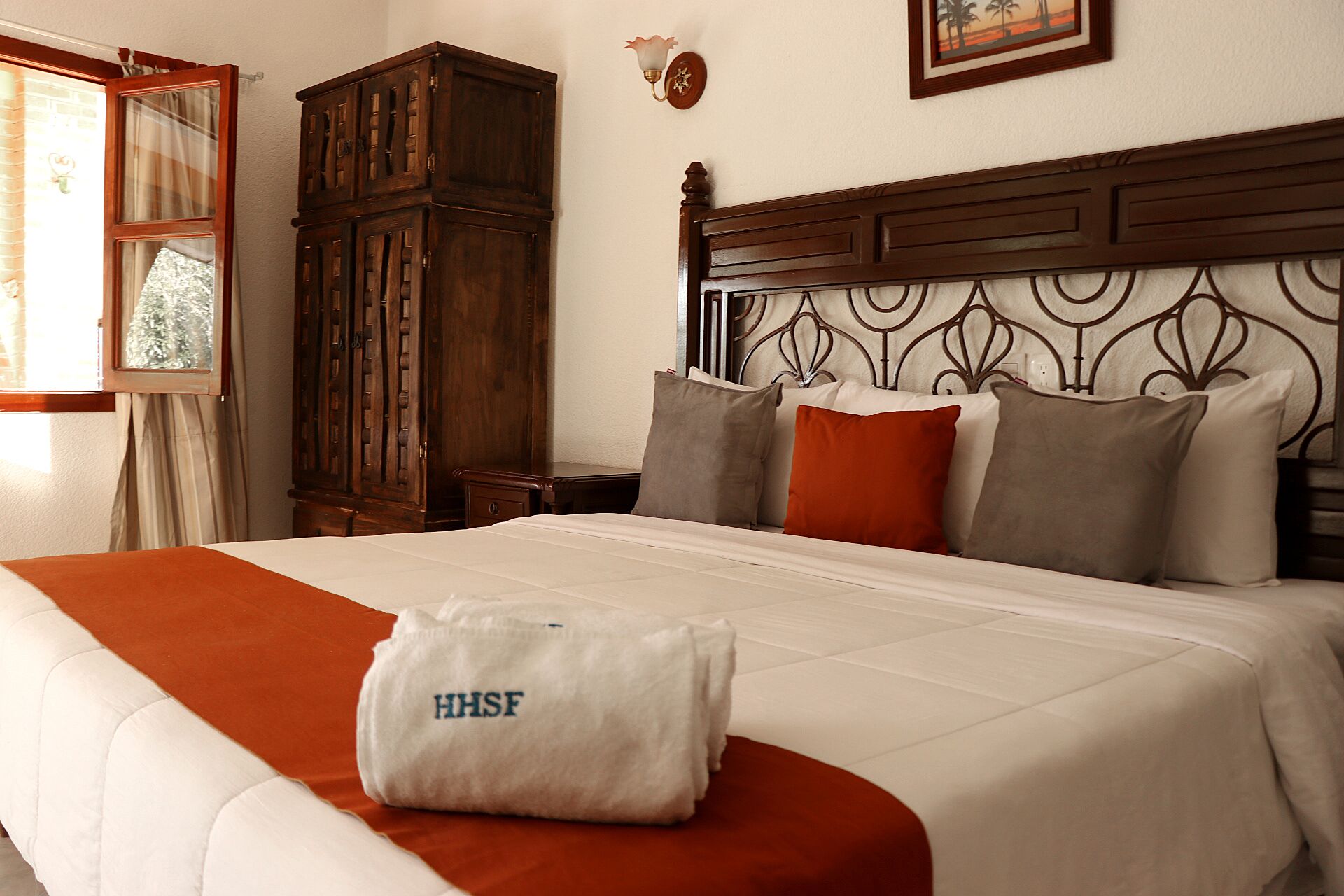 A hotel room with a bed, a wooden wardrobe, a nightstand, and a wall-mounted lamp.