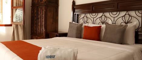 A hotel room with a bed, a wooden wardrobe, a nightstand, and a wall-mounted lamp.