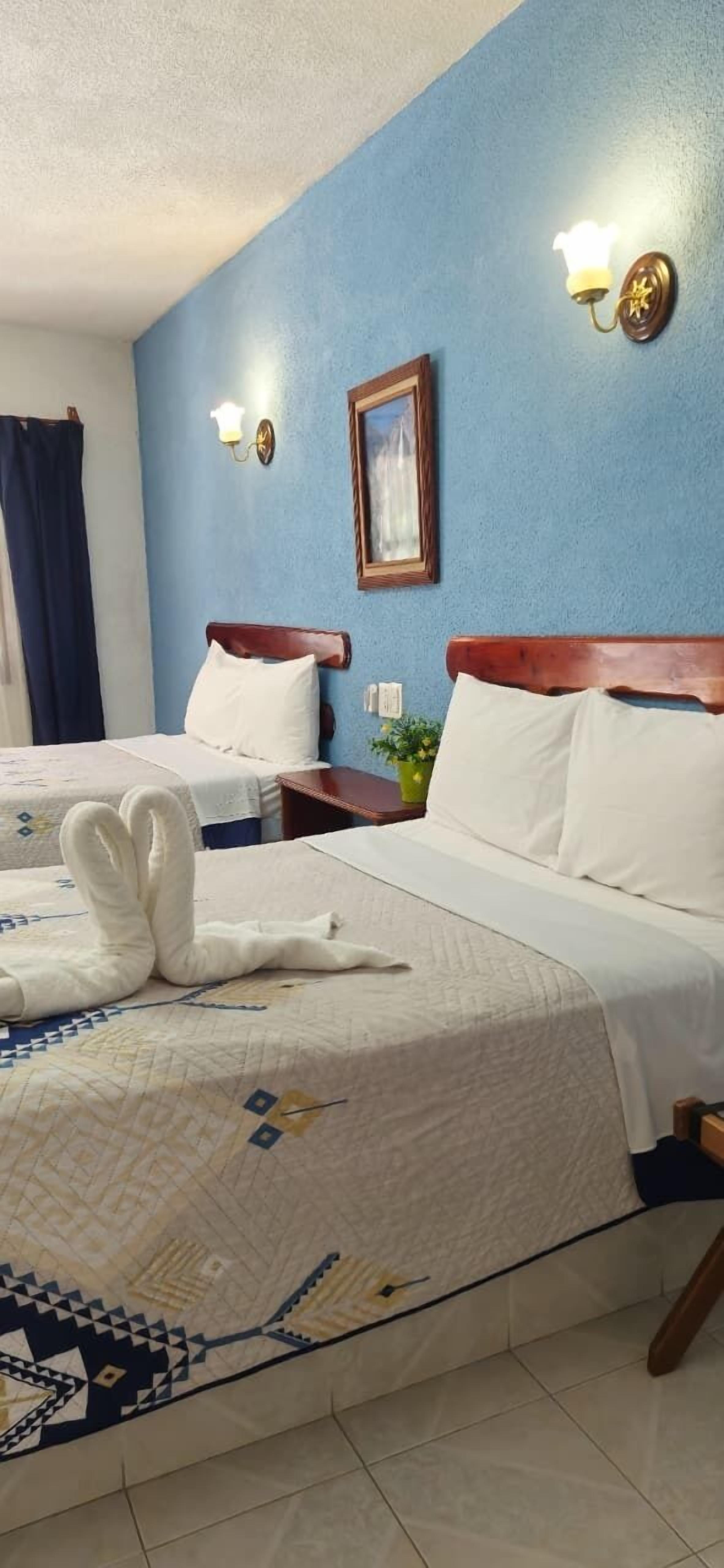 Une chambre d’hôtel avec deux lits, un mur bleu et un tableau encadré au-dessus de la tête de lit.