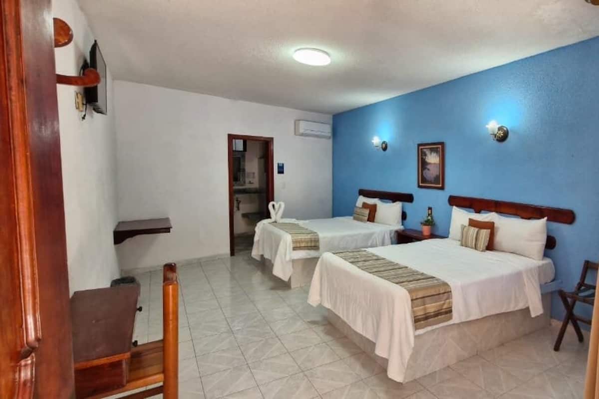 A hotel room with two beds, a wooden chair, a small table, and a blue wall.