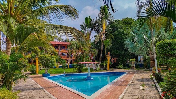 A swimming pool surrounded by palm trees and a building with a red roof. - Hotel HF Hacienda San Francisco (Paso de Ovejas)