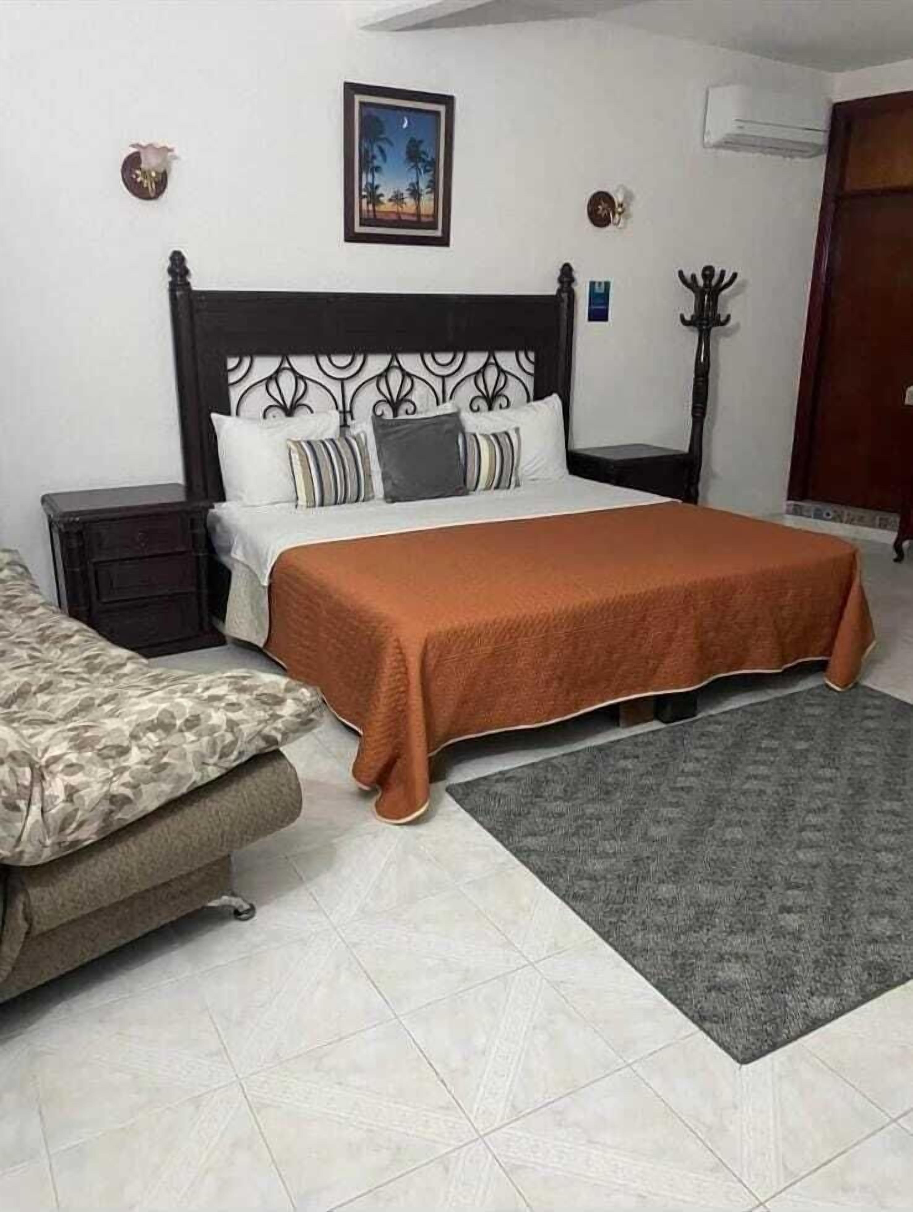 Une chambre à coucher avec un lit, une table de chevet, une chaise, un tapis et un tableau accroché au mur.