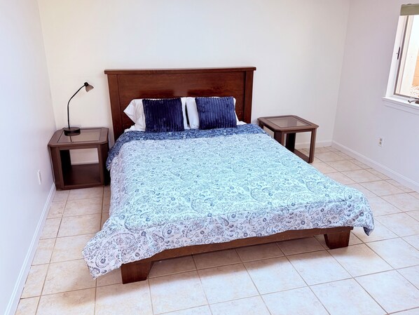 Un dormitorio con una cama de madera, dos mesitas de noche, una lámpara y una ventana.