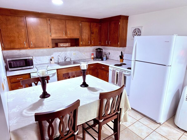A kitchen with wooden cabinets, a white refrigerator, a microwave, and a dining table with chairs. - Blue & White Getaway - 5 min to Beaver Stadium (State College)