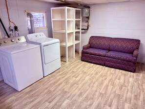 A laundry area with a washing machine and dryer, a white shelving unit, and a purple sofa. - Blue & White Getaway - 5 min to Beaver Stadium (State College)