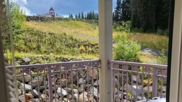 A wooden deck with a grill, a metal railing, and a view of a forested hillside. - Large Corner Condo in Creekside with a Patio to enjoy the Views  (Silver Star Mountain)