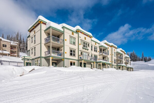 A multi-story hotel with balconies, snow-covered roofs, and a ski slope in the background.