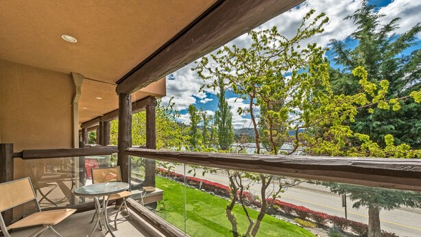 Un balcon avec une table et des chaises, donnant sur une route bordée d’arbres et un ciel dégagé.