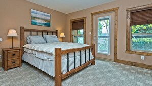 Une chambre à coucher avec un lit en bois, deux tables de chevet, une commode, une fenêtre avec des stores et une porte.
