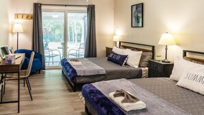 Hotelkamer met twee bedden, een bureau en een stoel. Er is een balkon met uitzicht op bomen.