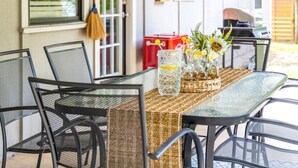 Een glazen tafel met een geweven tafelkleed, omringd door zwarte metalen stoelen.