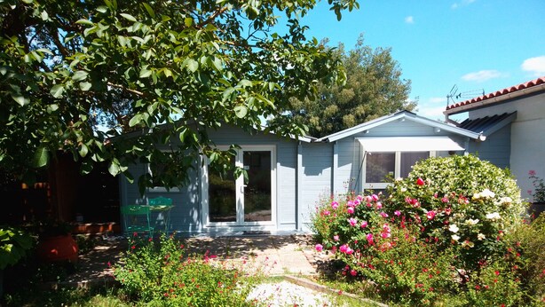 Una casa con puerta principal, un pequeño porche y un jardín lleno de plantas y flores.
