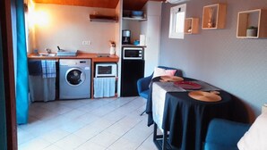 Cocina compacta con lavadora, microondas y un pequeño comedor con mesa y sillas.
