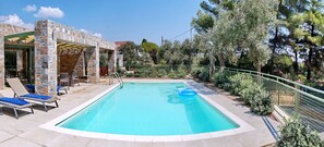 A swimming pool with lounge chairs, a stone structure, and surrounding greenery. - Ouzo Stone House 2, with private pool (Lesvos)