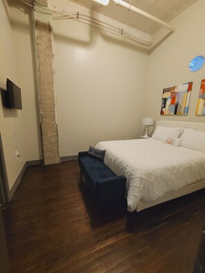 A bedroom with a large bed, a bench, a TV, and a wall with abstract art. - Rustic Realm/2BR2Bath/KayBaileyCenter/Pool/GYM (Dallas)