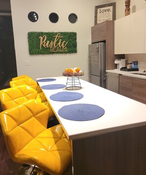 A kitchen with a central island, yellow chairs, and a rustic-themed wall decoration. - Rustic Realm/2BR2Bath/KayBaileyCenter/Pool/GYM (Dallas)