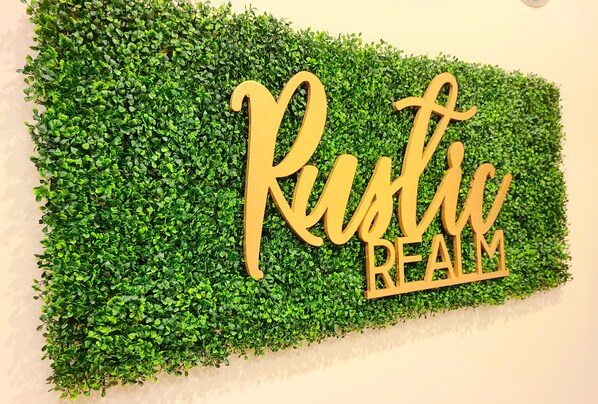 A wall with a green hedge and the words "Rustic Realm" in wooden letters. - Rustic Realm/2BR2Bath/KayBaileyCenter/Pool/GYM (Dallas)