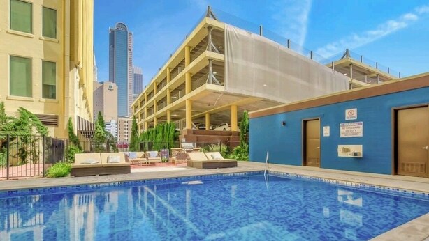 A swimming pool with lounge chairs and a covered area, surrounded by buildings and a clear sky. - Rustic Realm/2BR2Bath/KayBaileyCenter/Pool/GYM (Dallas)