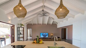 A spacious kitchen with a central island, a dining area with a table and chairs, and a television in the background. - Villa Seven - Coral Estate, Spectacular Views - Ocean Access ! (Curaçao)