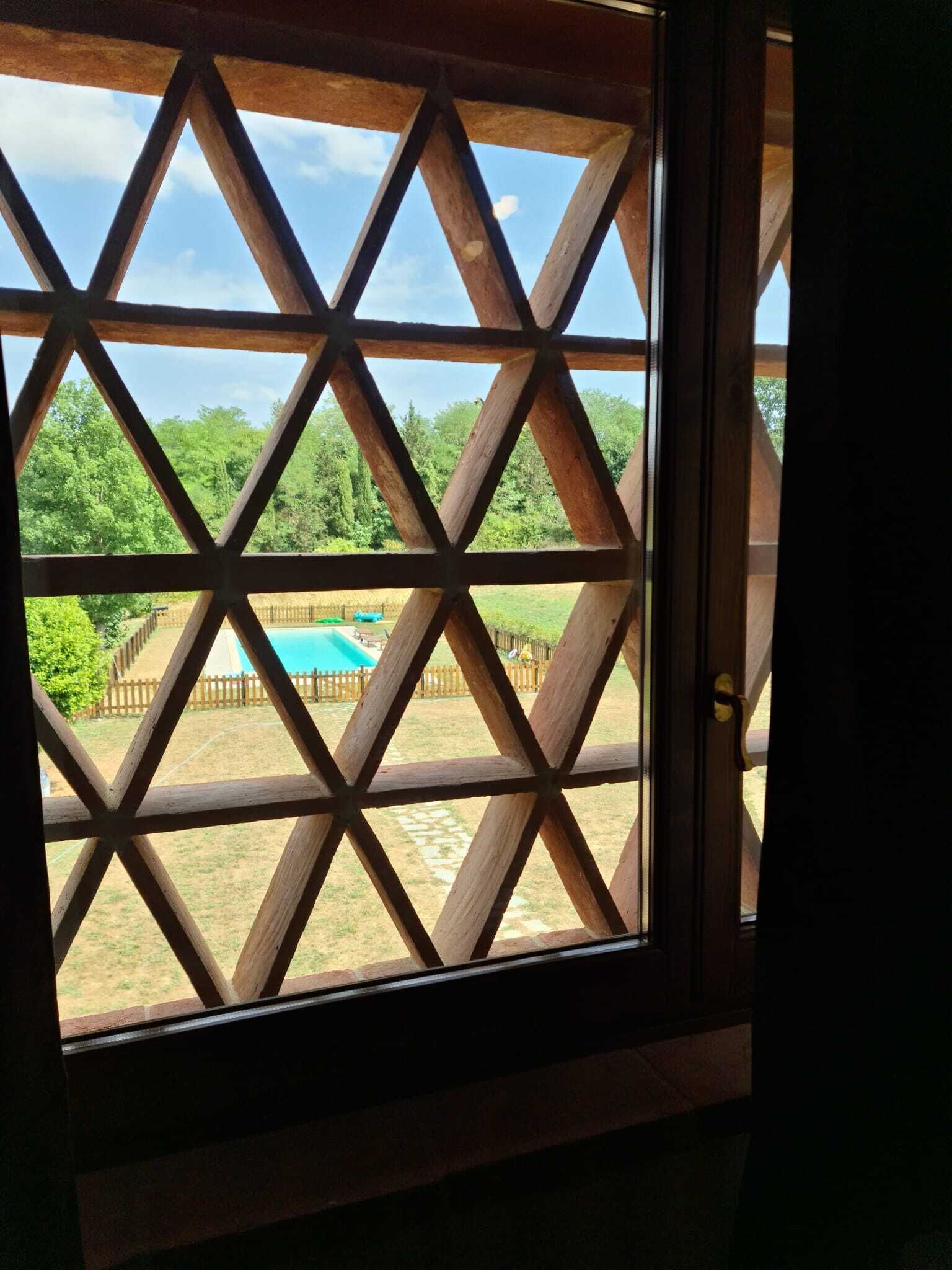 A view through a wooden lattice window with a pool and greenery visible outside.