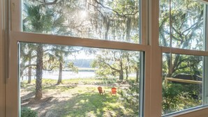 Blick durch ein Fenster auf einen grünen Garten mit Bäumen und einem See.