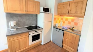 Une cuisine compacte dotée de meubles en bois, d’un four à micro-ondes, d’une machine à café, d’un lave-vaisselle et d’un dosseret carrelé.