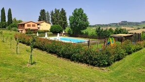 A pool area with a wooden fence, a slide, and a tennis court.