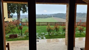 A covered patio with a view of a green landscape and a wooden fence.