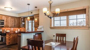 Una cocina con armarios de madera, una mesa de comedor con sillas, una araña y una ventana con vistas.