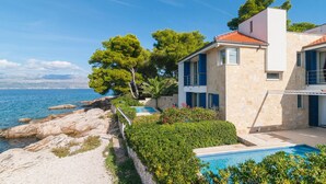 En villa vid kusten med en swimmingpool, stenmurar och utsikt över havet.