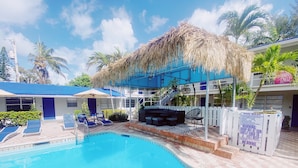 A swimming pool with lounge chairs and a thatched roof structure. - Sea Steps by Lowkl (Pompano Beach)