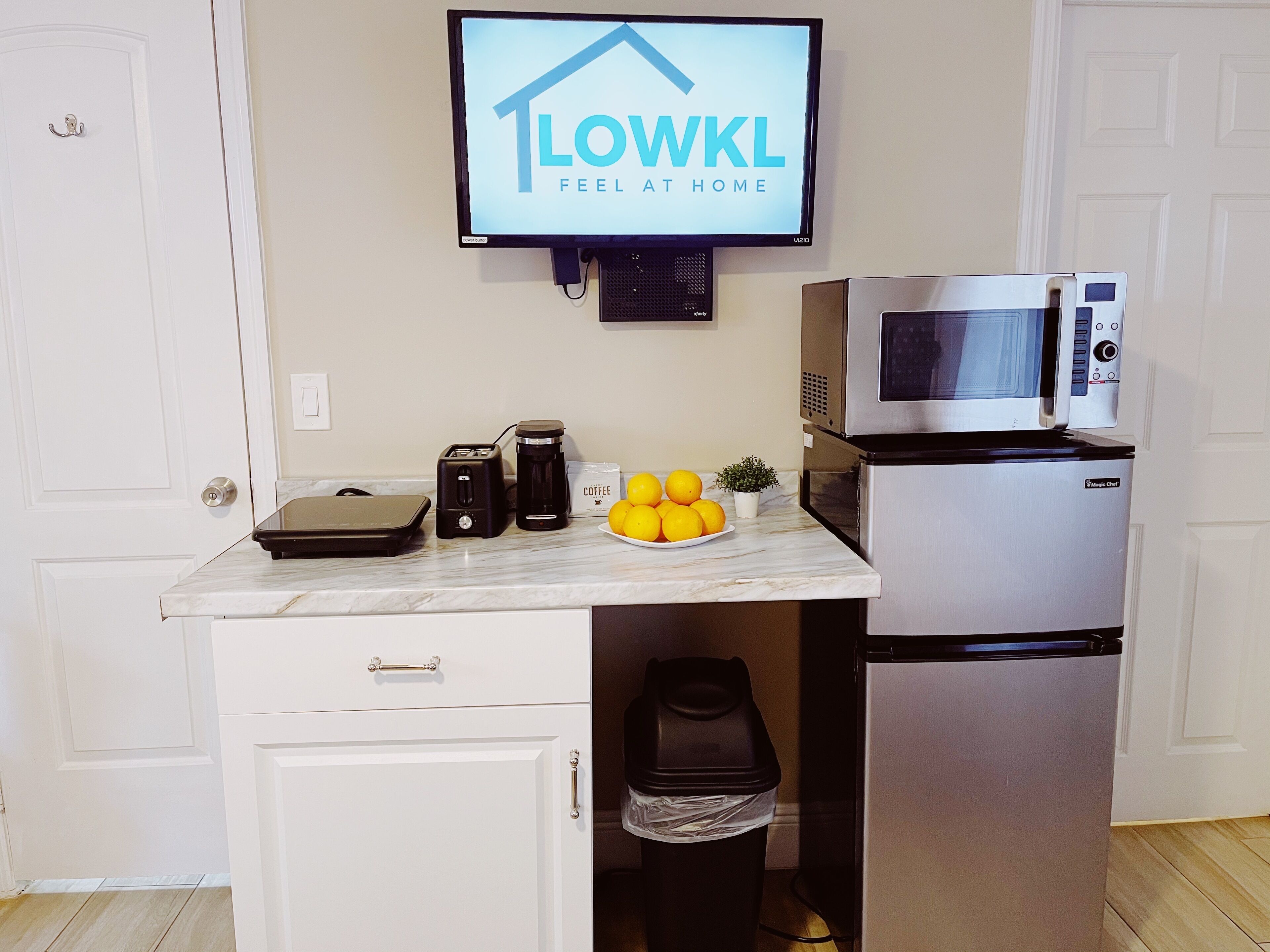 A compact kitchen with a microwave, toaster, coffee maker, and a bowl of lemons on the counter.
