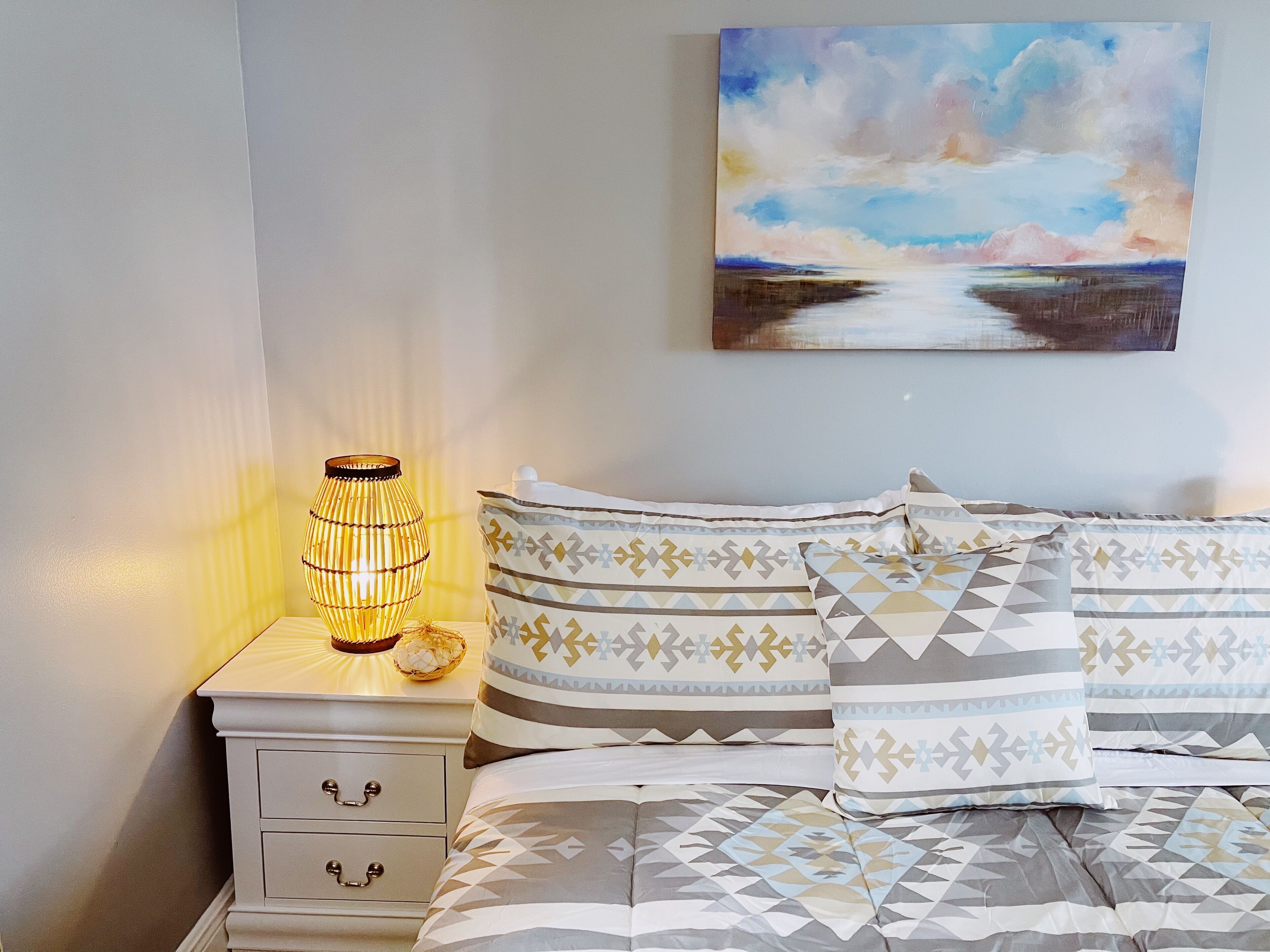 A neatly made bed with patterned pillows and a bedside table with a lamp and decorative bowl.